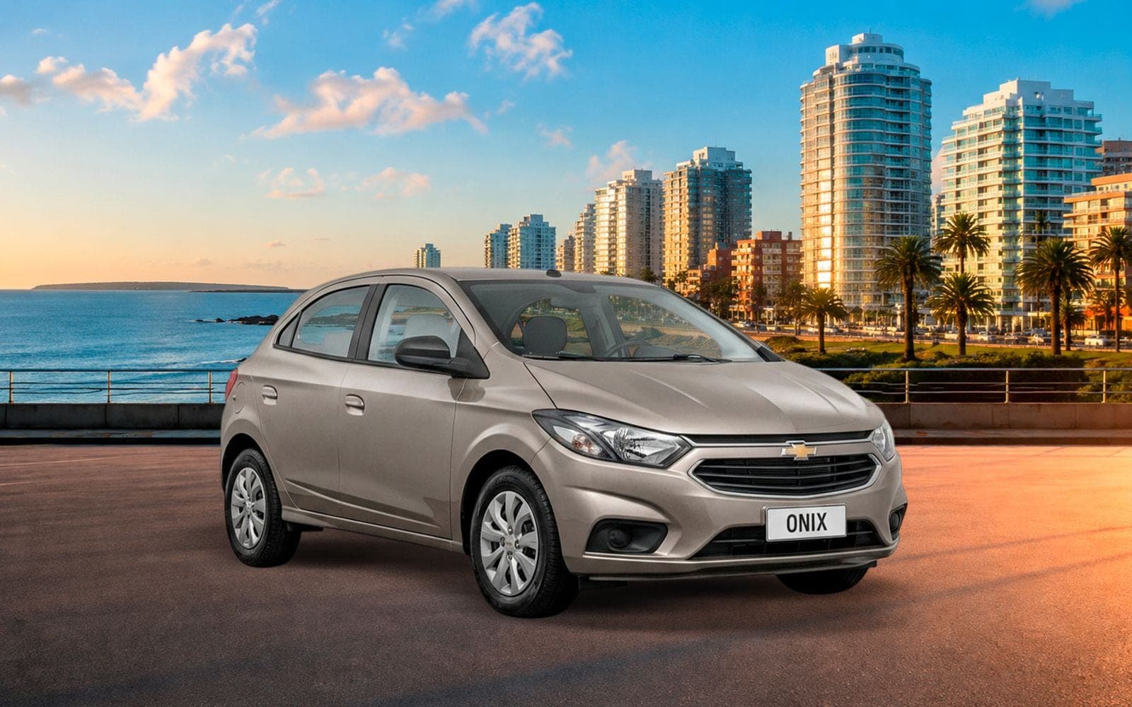 Chevrolet Onix beige de cinco puertas, de frente y tres cuartos, con la playa y los edificios de la costa de Montevideo detrás